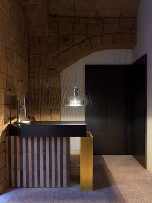 Un interior moderno con pared de piedra, mostrador de recepción negro, lámpara colgante y puerta oscura.