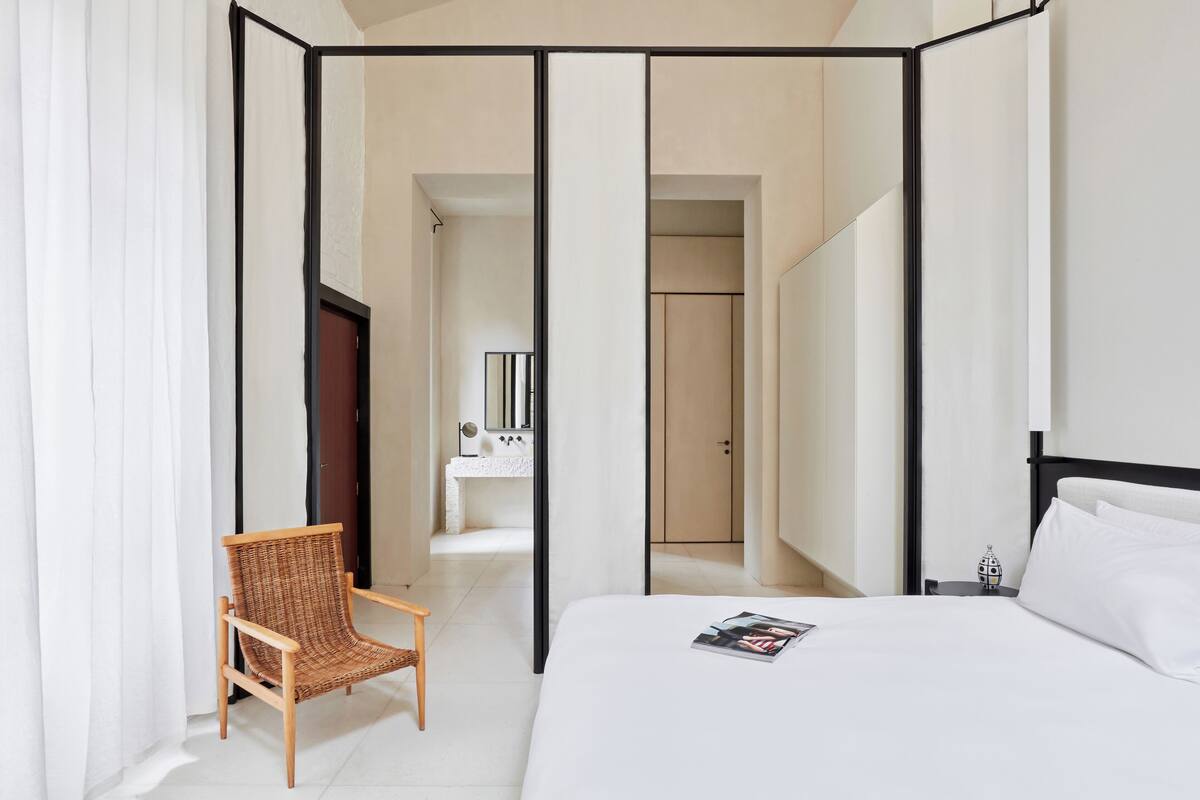 A hotel room with a bed, a chair, a wardrobe, and a bathroom visible through a sliding door.