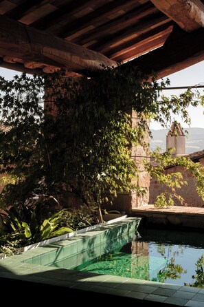 Zona de piscina con muro de piedra y vista a una torre distante.