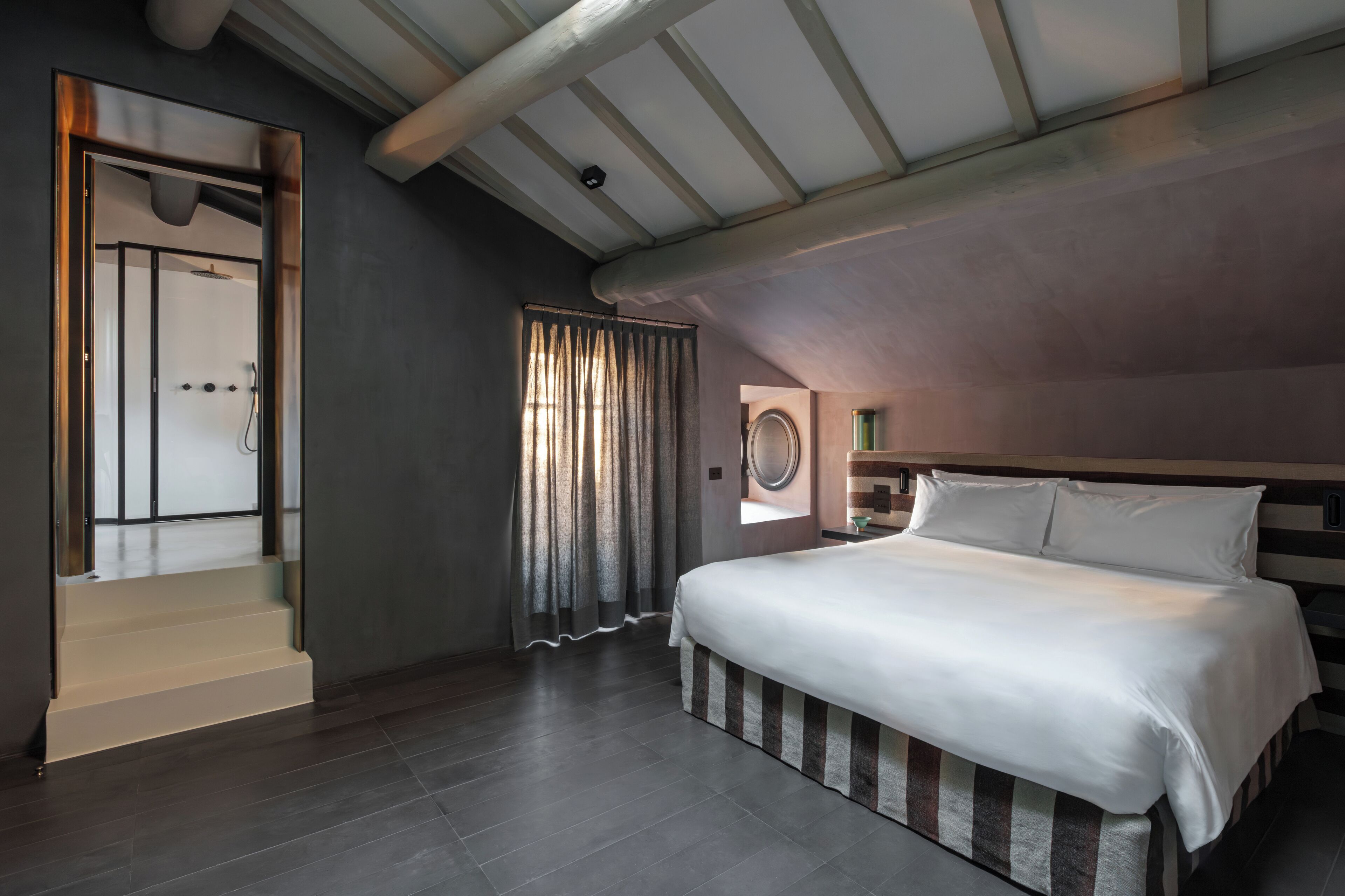 A modern bedroom with a large bed, a built-in shower, and a view of the outdoors through a window.