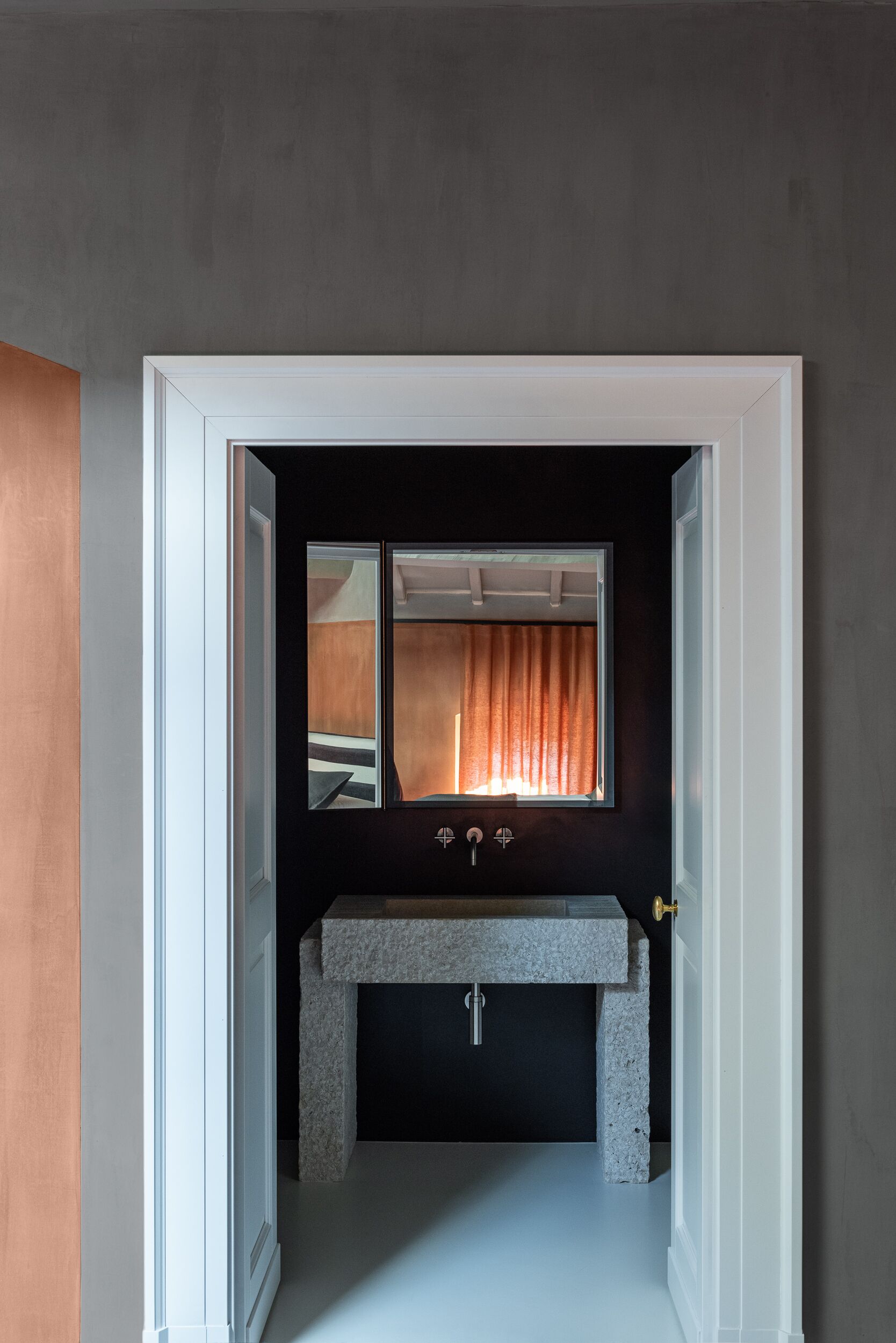 A bathroom with a dark wall, a white door, a window with curtains, and a granite sink.