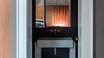 A bathroom with a dark wall, a white door, a window with curtains, and a granite sink.