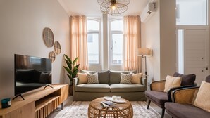 A modern living room with a flat-screen TV, a sofa, a coffee table, and a wicker ottoman.