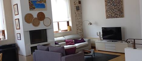 Una sala de estar con chimenea, un sofá, un televisor y una pared de piedra.