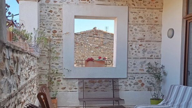 Un espace extérieur aménagé avec des murs en pierre, comprenant deux chaises en métal, un canapé et une petite table.