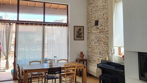 Un vaste salon agrémenté d’un mur en pierre, d’une cheminée, d’un coin repas avec des meubles en bois et d’une grande fenêtre avec des rideaux.