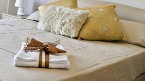 Ein ordentlich bezogenes Bett mit einem weißen und braunen Handtuch, einem flauschigen weißen Kopfkissen und einem gemusterten Kissen.