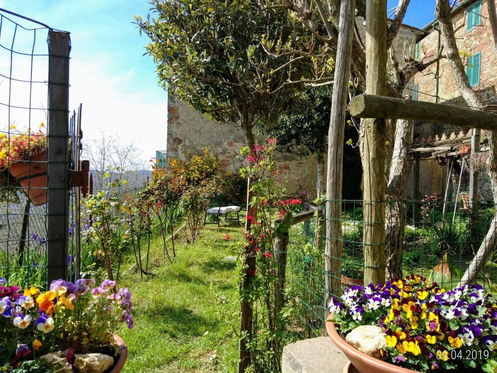 A garden with potted flowers, a rustic building, and a metal fence.