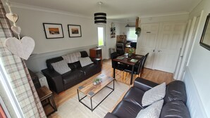 Una sala moderna con un sofá de cuero negro, una mesa de centro de madera y un comedor con mesa y sillas de madera.