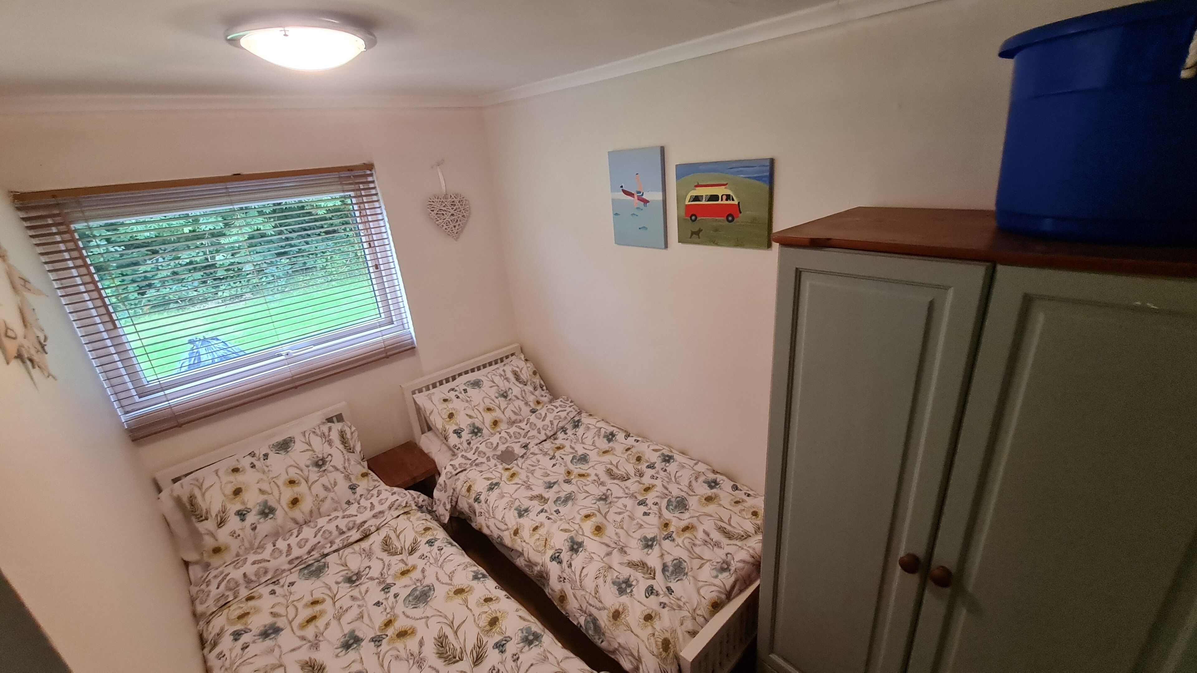 Una habitación con dos camas individuales, una ventana con persianas, un armario y dos pequeñas obras de arte en la pared.