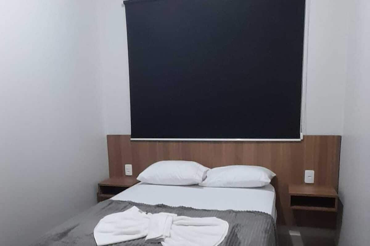 A hotel room with a bed, a flat-screen TV mounted on the wall, and a bedside table with a lamp.