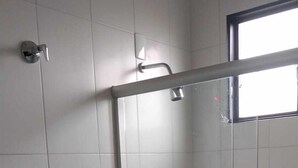 Une salle de bain moderne avec une douche à parois de verre, des toilettes blanches et un petit coin lavabo.
