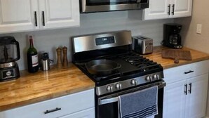 A modern kitchen with white cabinets, a stainless steel microwave, a gas stove, and a coffee maker. - New! Renovated 2BD Home in Downtown (Billings)