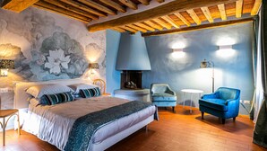 Ein Schlafzimmer mit einem Bett, einem blauen Sessel, einem kleinen Tisch und einem Kamin.