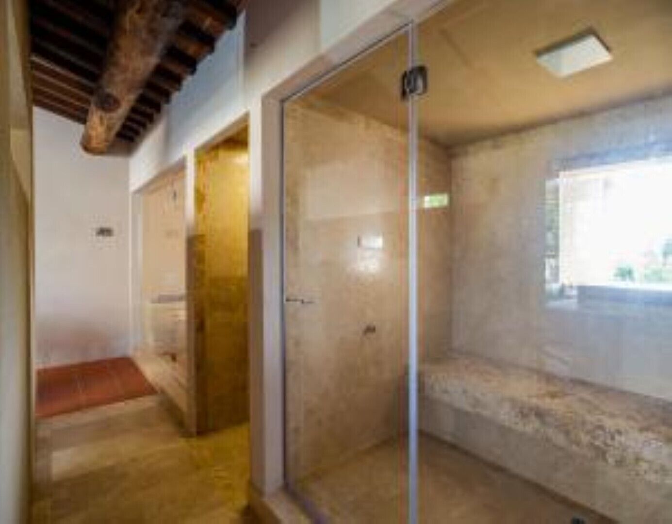 A room with a glass shower enclosure, a wooden ceiling, and a window providing natural light.