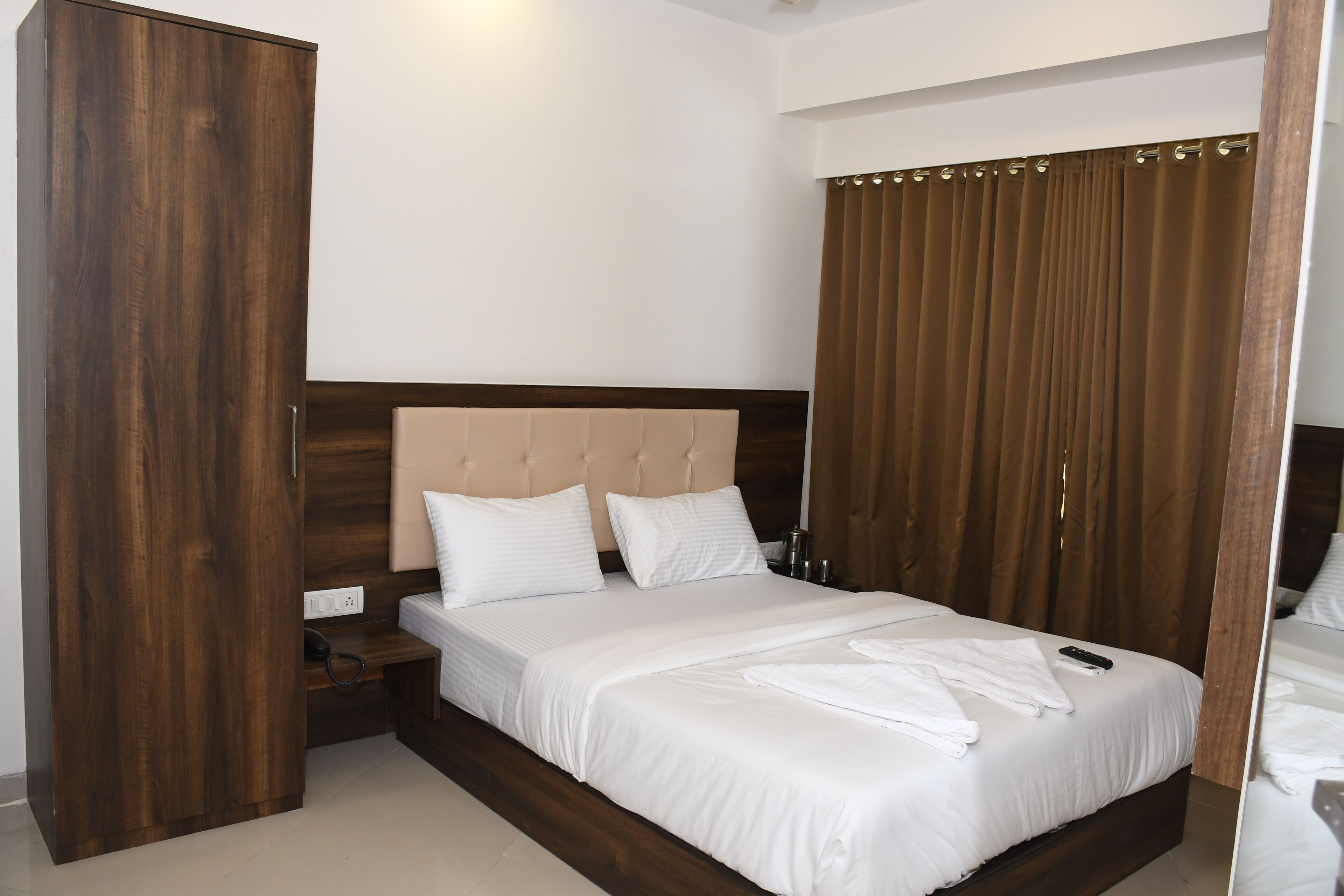 A bedroom with a large bed, a wooden wardrobe, a bedside table, and a curtain.