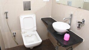 Kylpyhuone, jossa on valkoinen wc-istuin, musta pesuallas, peili ja suihku.