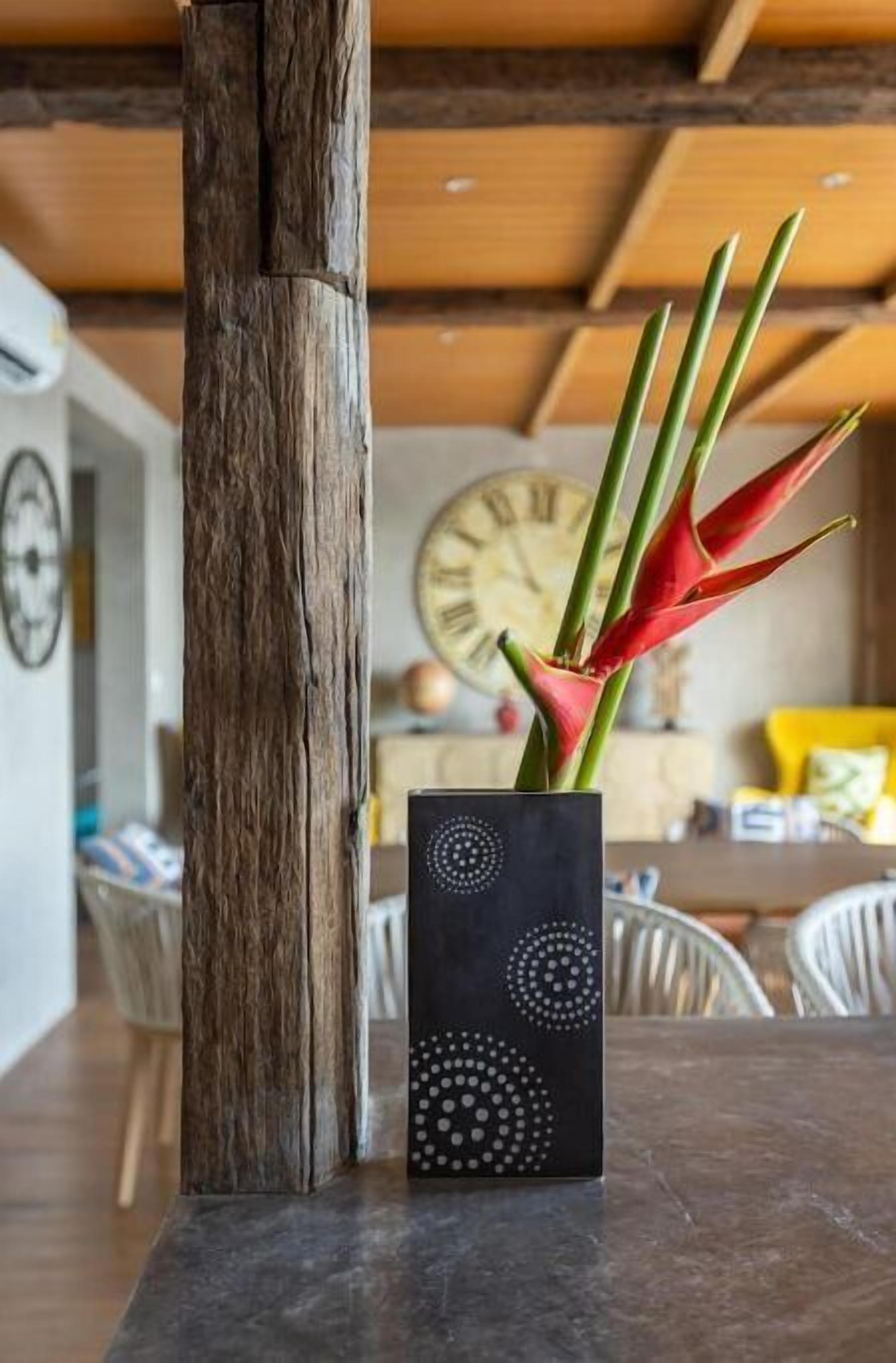 A wooden pillar, a black vase with white patterns, and a red and green plant in a modern interior setting.