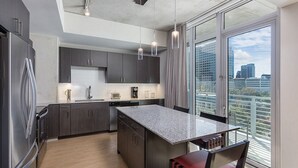 A modern kitchen with dark cabinets, a granite countertop island, and a large window offering a city view. - 2BD/Austin - Full Kitchen, W/D, Balcony, Fire Pit! (Austin)