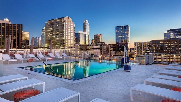 A rooftop pool with lounge chairs and a city skyline in the background. - 2BD/Austin - Full Kitchen, W/D, Balcony, Fire Pit! (Austin)