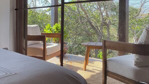 A room with a bed, a wooden table, and two chairs. There is a large window with a view of trees and a wooden ceiling. - A Remote Paradise in nature - Villa - Ocean View (Pedasi)