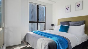 Een hotelkamer met een groot raam, een bed met wit- en blauwe beddengoed, en twee ingelijste decoratieve wandpanelen.