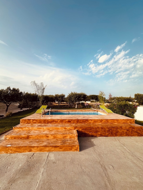 A swimming pool with wooden steps and a clear blue sky.