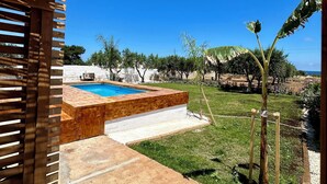 A wooden pergola with a pool area, including a concrete deck and a small garden with a banana tree. - VILLA Indipendente con Piscina privata e accesso al mare. (Puglia)