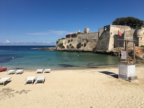 A beach with white lounge chairs, a stone wall, and a flag. - VILLA Indipendente con Piscina privata e accesso al mare. (Puglia)