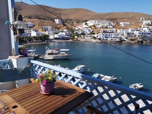 A balcony with a wooden table and potted flowers, overlooking a marina with boats and white buildings on a hillside.