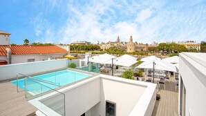 A rooftop pool with glass railings, outdoor seating, and a view of historic buildings in the background. - Genteel Home Betis XXVI (Seville)