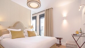 Quarto de hotel com uma cama grande, uma mesa pequena, uma cadeira e vista para o exterior.