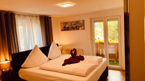 A hotel room with a bed, two pillows, a red towel, a painting of a car, and a view of greenery through a sliding door. - 87452 Altusried district Frauenzell, near Center Parcs Leutkirch im Allgäu (Altusried)