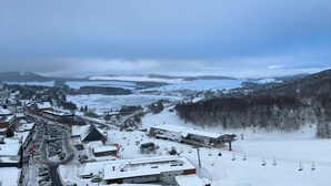 A snow-covered ski resort with a ski lift, buildings, and a mountainous backdrop. - 7 Couchages + Bébé, sur les Pistes + Parking (Besse-et-Saint-Anastaise)