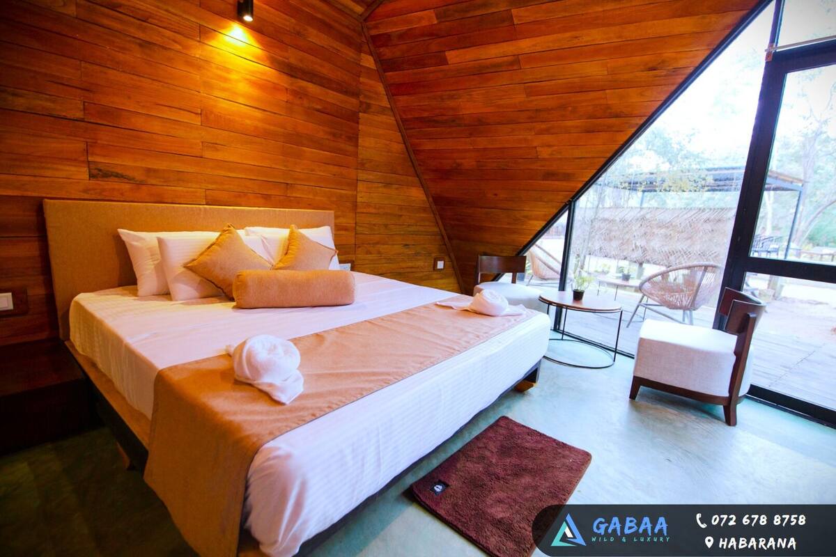 A bedroom with a wooden ceiling, a bed with white linens, a small table, and a chair.