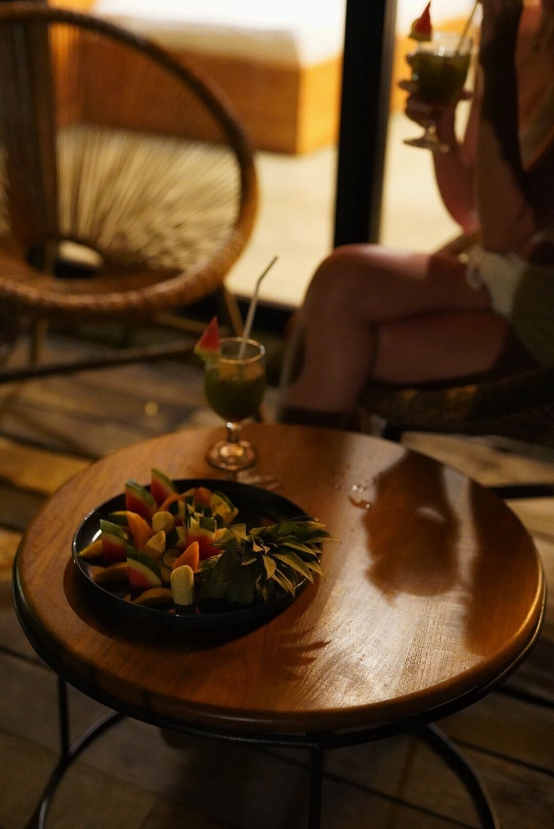A dining table with a plate of fruit salad and a cocktail on it.