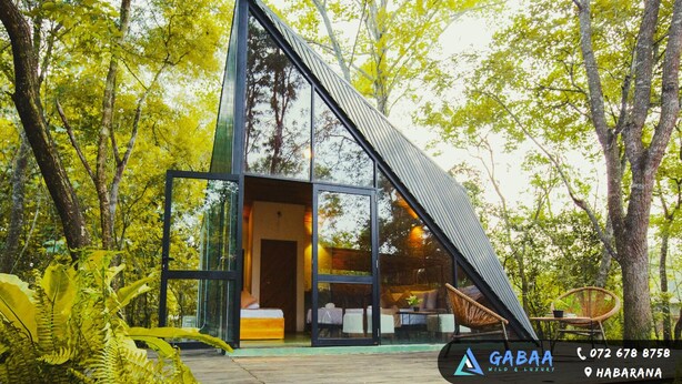 Eine moderne, gläserne Holzhütte im Wald, mit sichtbarem Bett und Sitzbereich.