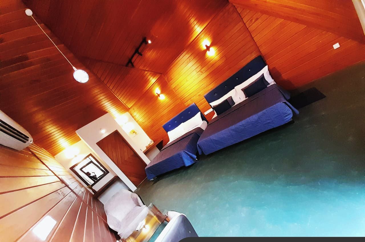 A hotel room with wooden ceilings, two beds with blue and white bedding, a small table, and a mirror.
