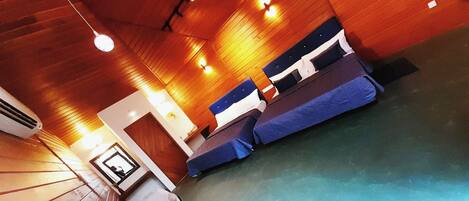 A hotel room with wooden ceilings, two beds with blue and white bedding, a small table, and a mirror.