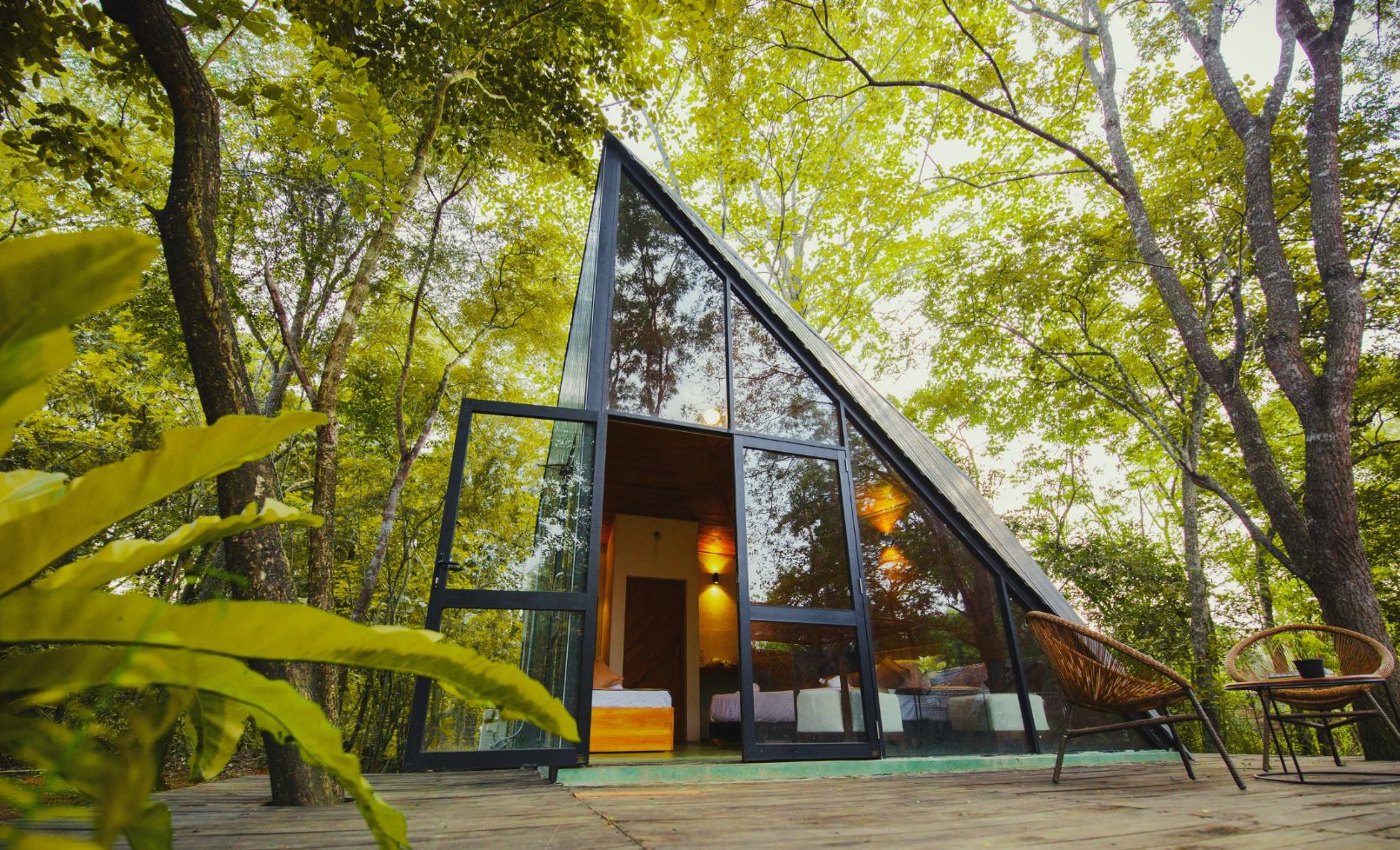 A modern glass house with a triangular roof, surrounded by lush green trees.
