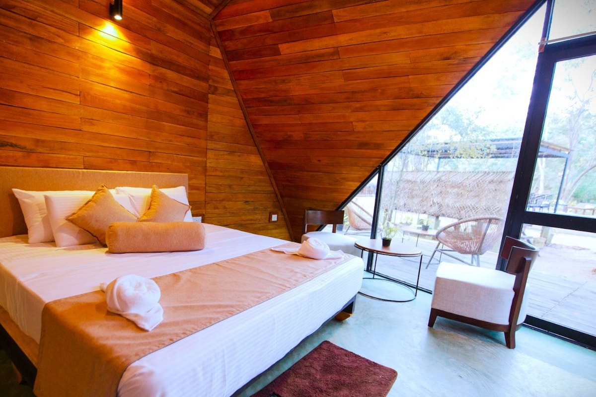 A bedroom with a wooden ceiling, a bed with white linens, a small table, and a chair.