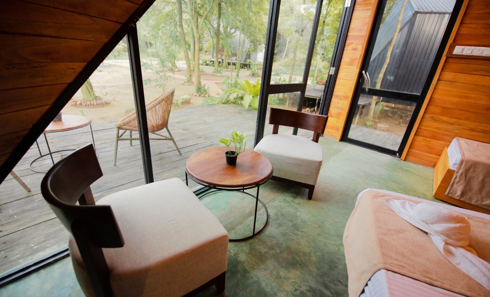 A cozy room with a wooden ceiling, a round table with a plant, two chairs, and a bed.