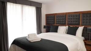 A neatly made bed with a dark green and white duvet, a folded white towel, and a wooden headboard with a tufted design. - ROZAS (Ezeiza)