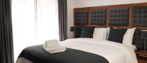 A neatly made bed with a dark green and white duvet, a folded white towel, and a wooden headboard with a tufted design.
