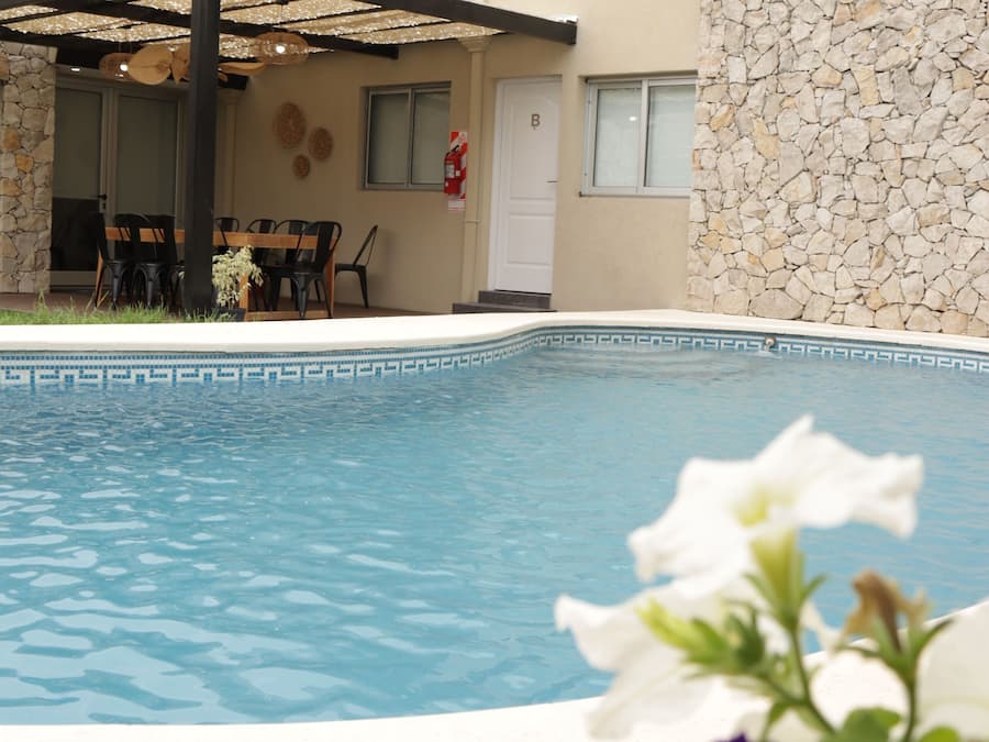 Una piscina con un muro de piedra y un porche cubierto.