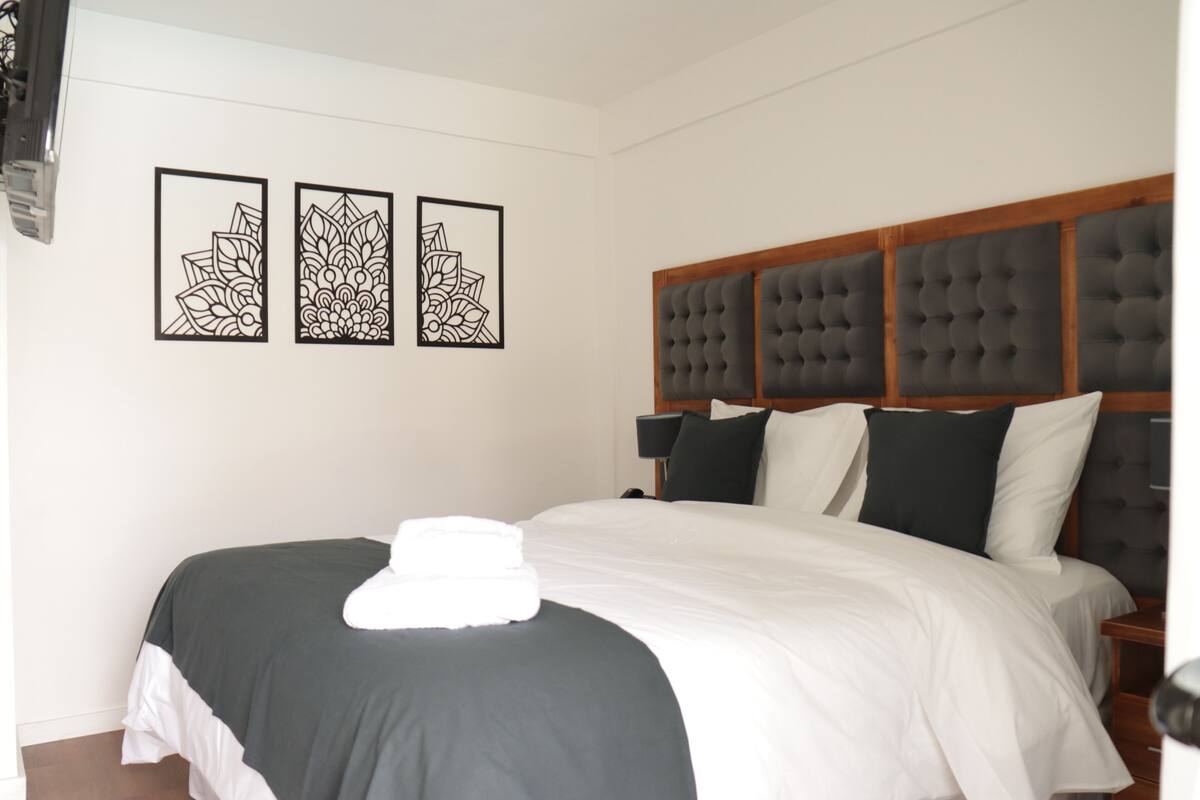A neatly made bed with a white and dark grey bedspread, a tufted headboard, and three framed wall art pieces.