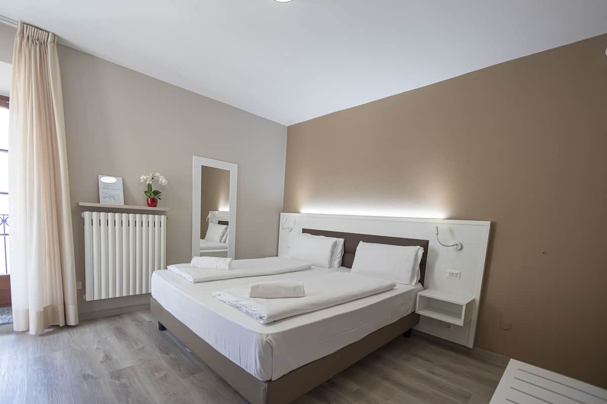 Une chambre moderne avec deux lits, une table de chevet, un miroir, un radiateur et une fenêtre avec des rideaux.