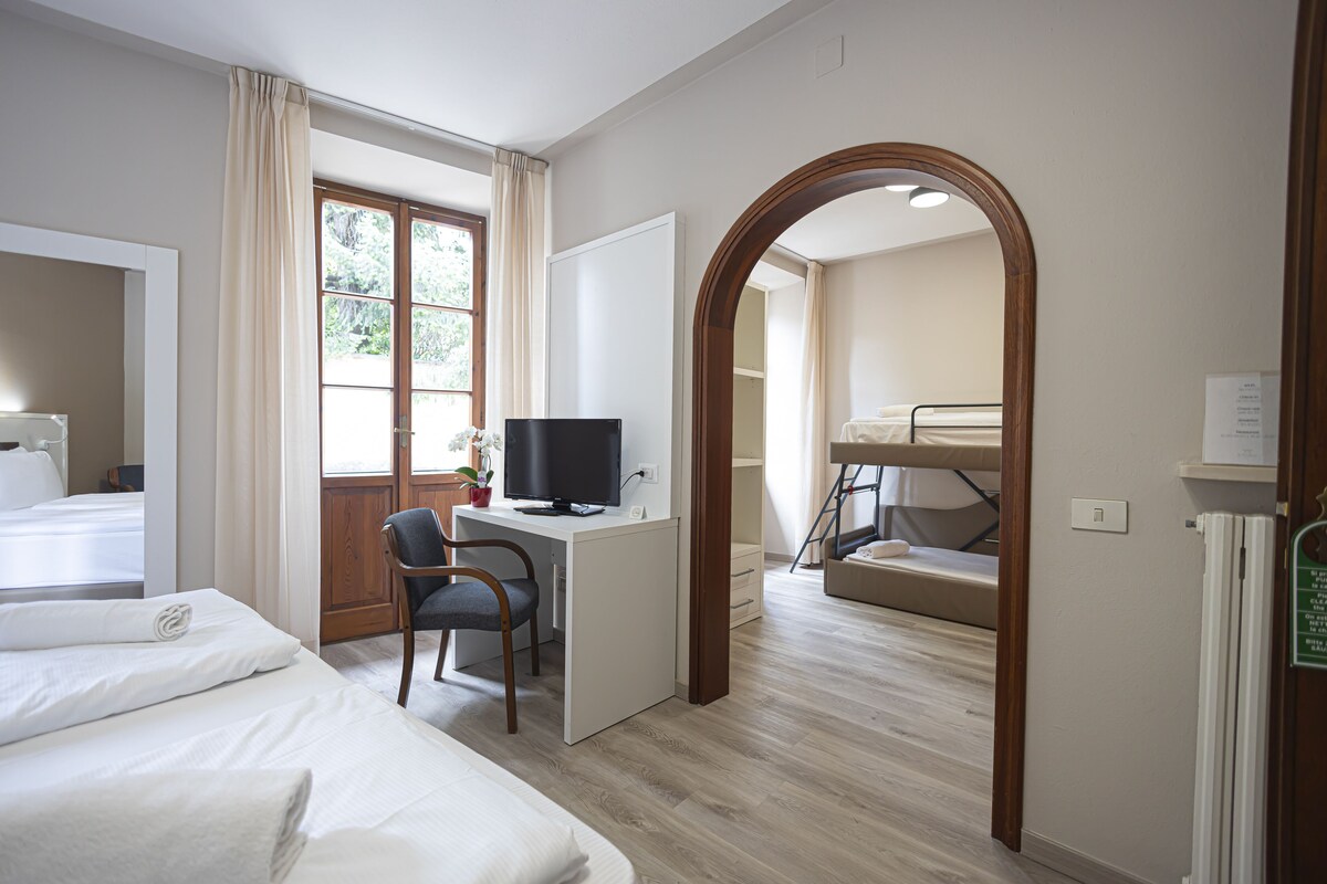 A hotel room with a bed, desk, chair, television, and a view of the outdoors through a window.