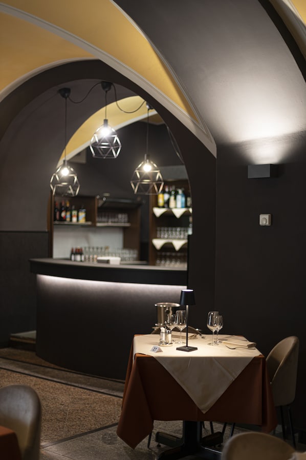 A restaurant with a bar area, tables set with glasses and cutlery, and a modern geometric light fixture.