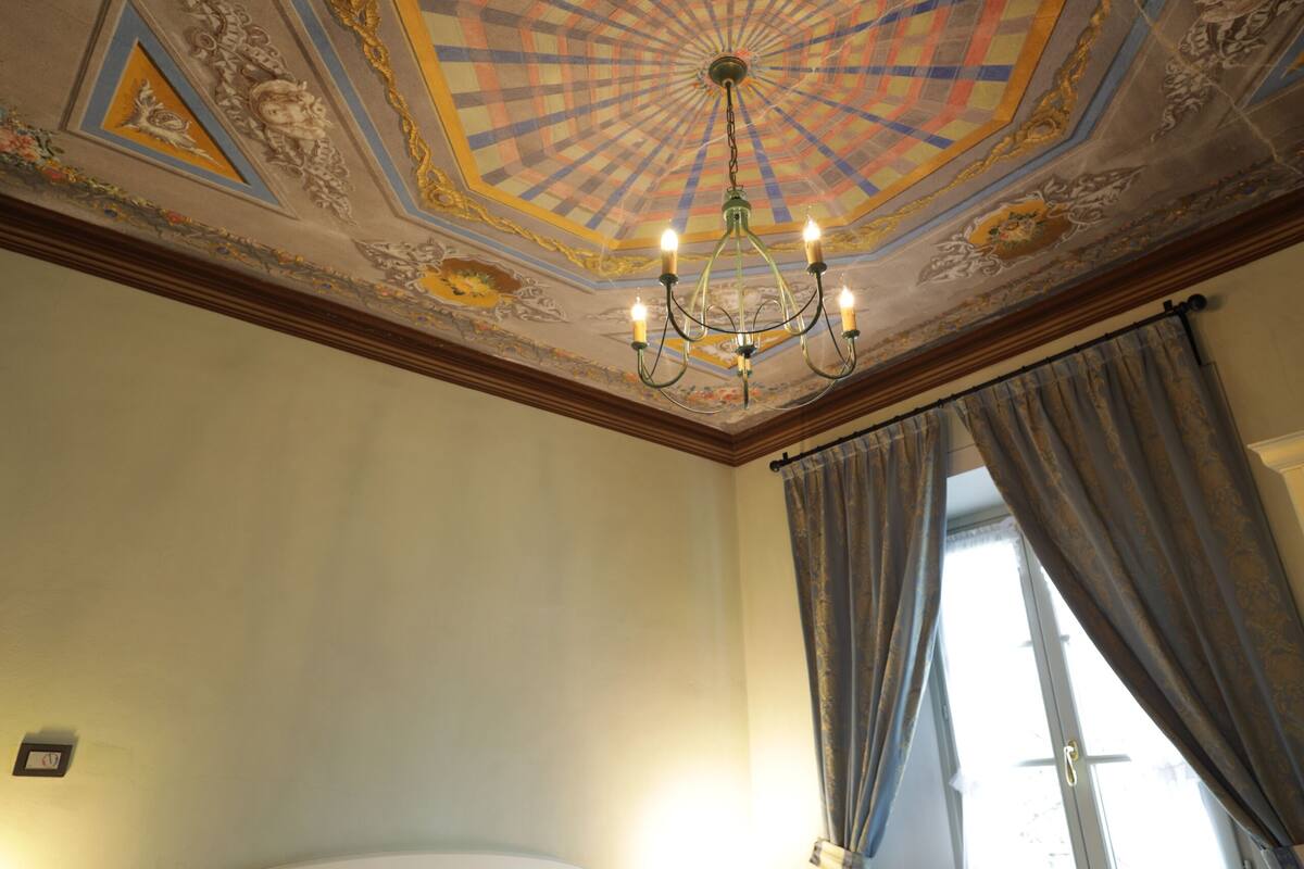 Une chambre d’hôtel avec un grand lit, un lustre et un plafond orné de motifs complexes.